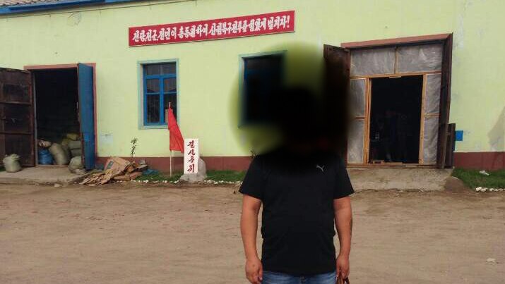 A man with his face blurred standing in front of a building in North Korea.