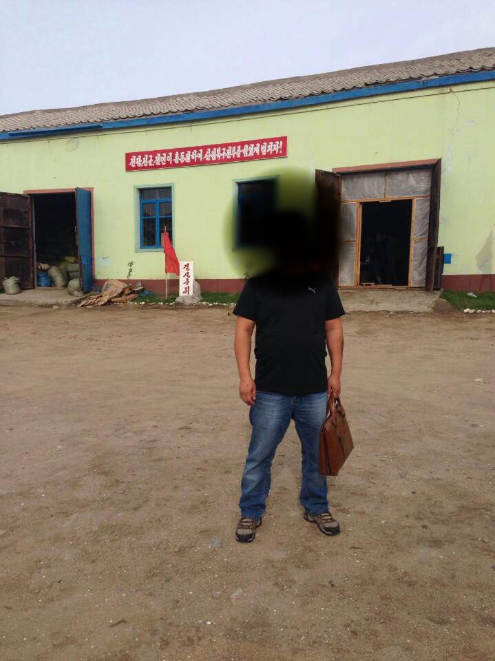 A man with his face blurred standing in front of a building in North Korea.