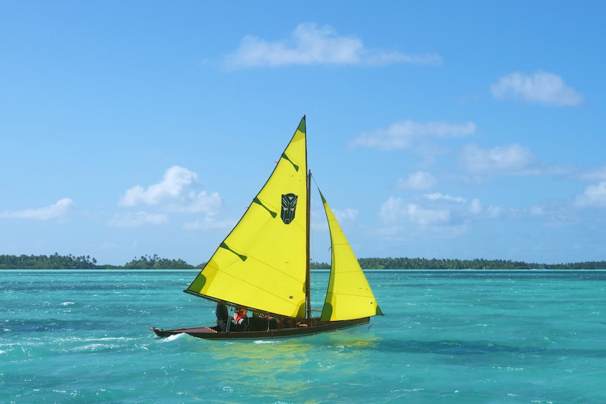 A wooden boat with bright yellow sails on turquoise water.