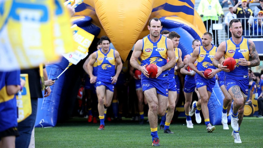 West Coast Eagles players run onto Perth Stadium from a tunnel before an AFL game.