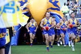 West Coast Eagles players run onto Perth Stadium from a tunnel before an AFL game.