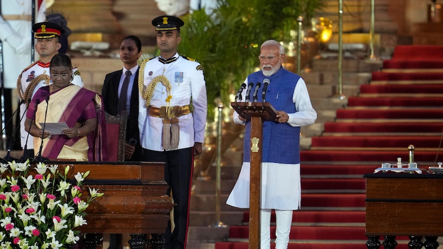 An Indian man is standing and speaking at a lectern. Next to him is a woman and two men in military uniform.