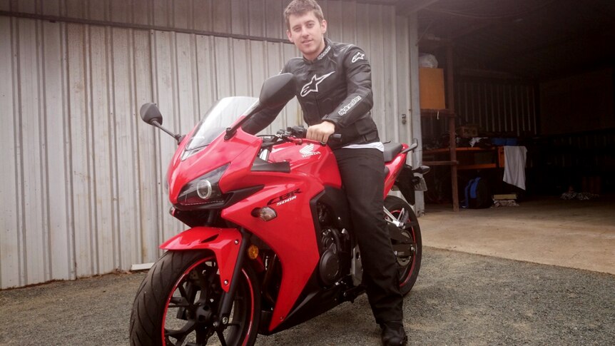 A young man on a red motorbike, smiling at the camera.