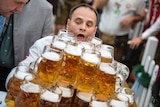 A man carrying a tray of 27 beer steins concentrates on not dropping them.