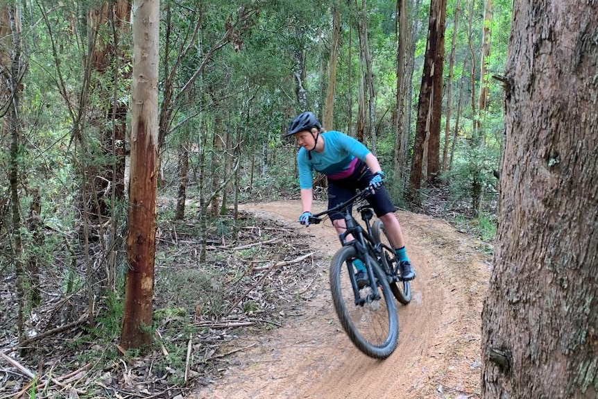 A woman rides a bike along a gravel track through a forest.