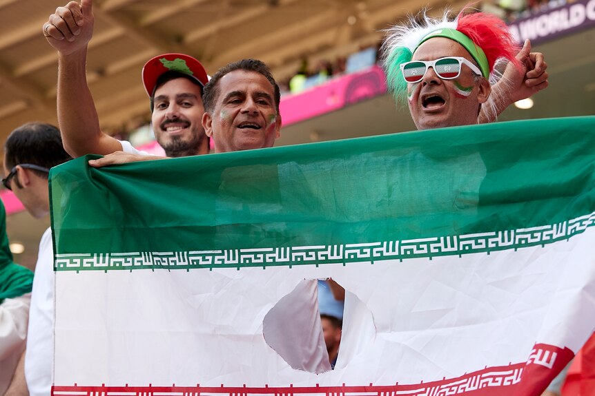 Fans hold an Iran flag with the centre symbol cut out of it