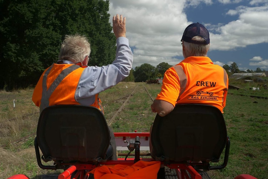 Two men riding a tandem bike along a railway track.