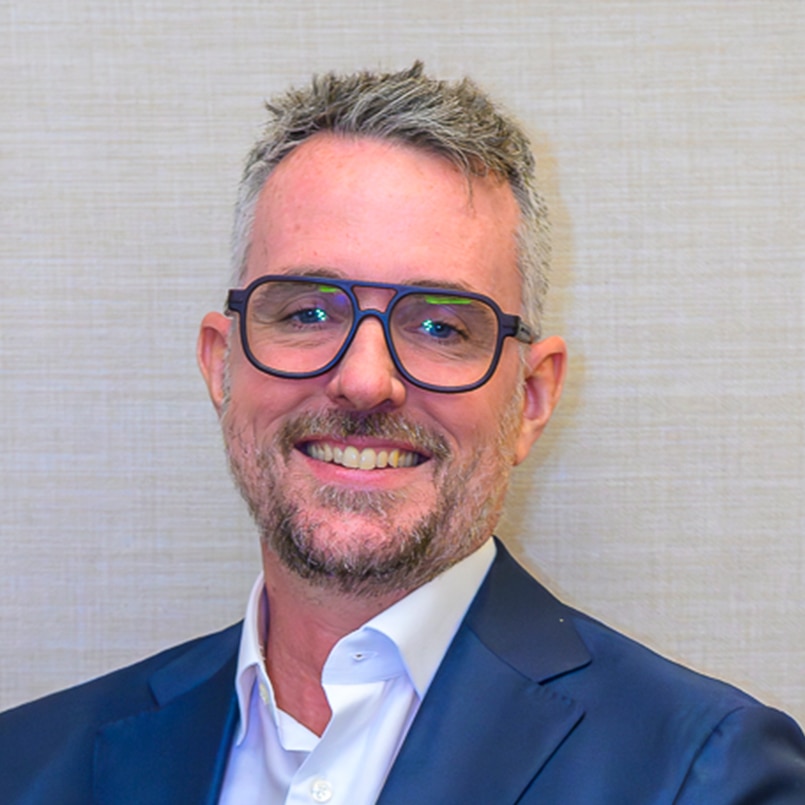A man with glasses and facial hair smiles for a headshot.