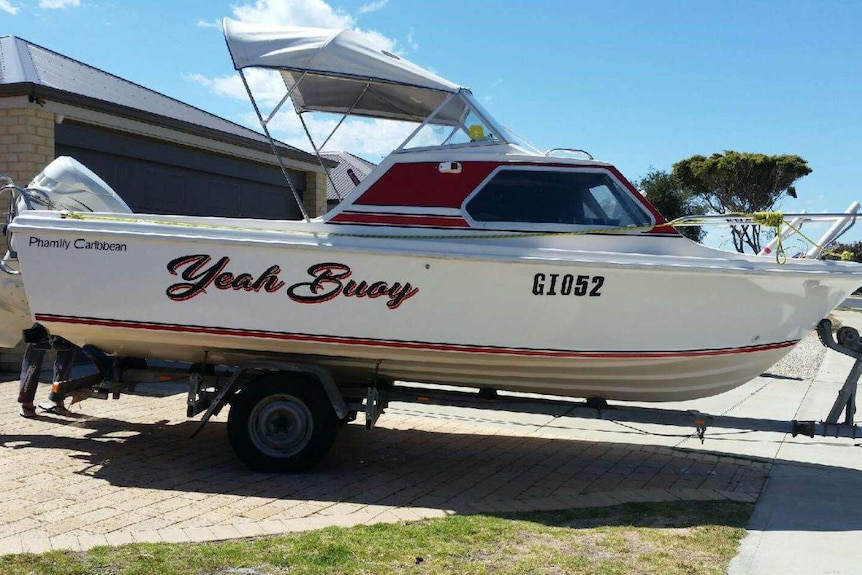 A white and red 5.5-metre boat with the name 'yeah Buoy' on the side sits on a trailer in the driveway of a house.