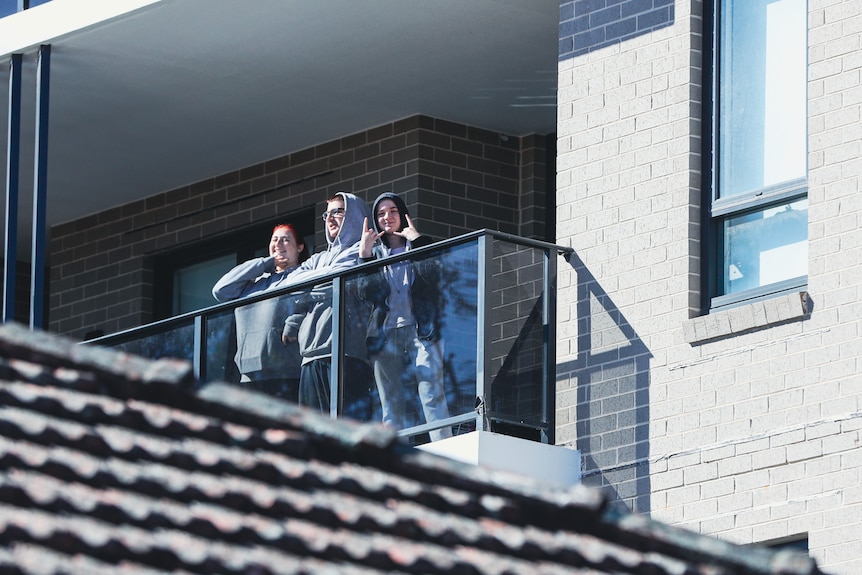 Three hooded people stand on apartment balcony