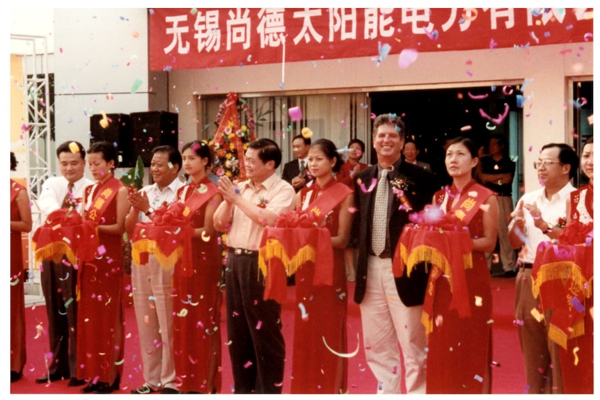 Women in matching red dresses and men in suits stand in a line as confetti rains down