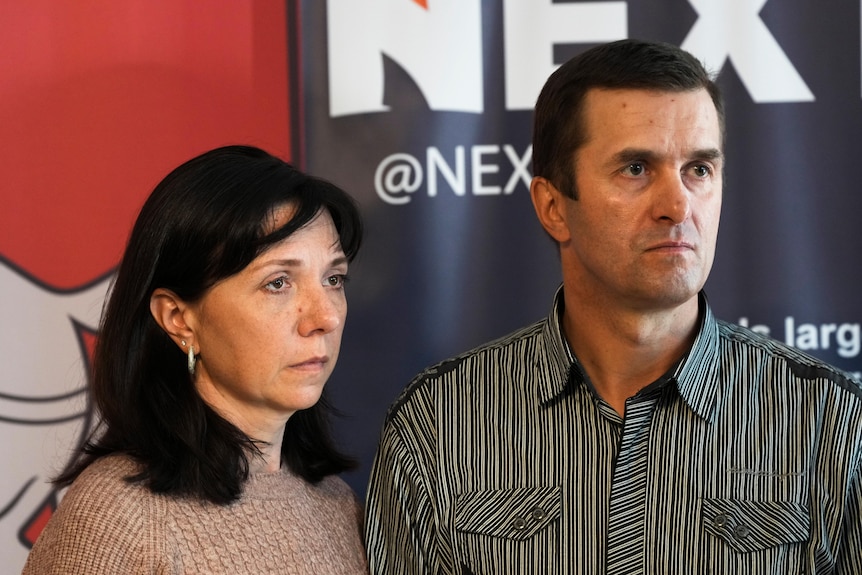 A woman and a man stand with concerned expressions on their faces