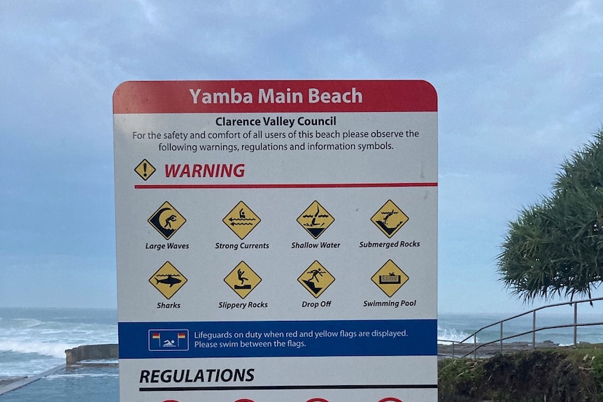 A warning sign with various symbols at a beach