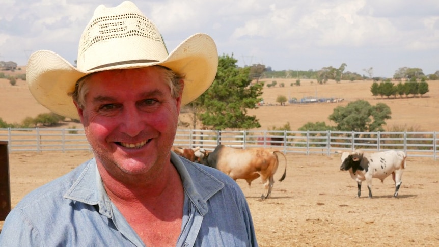 George Hempenstall smiling at the camera with his cattle in the background.