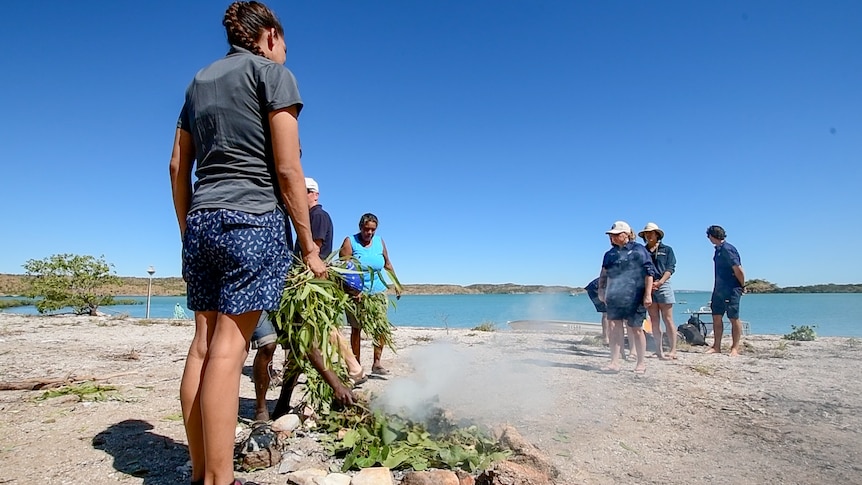 Six people on an isolated beach conducting a traditional smoking ceremony.