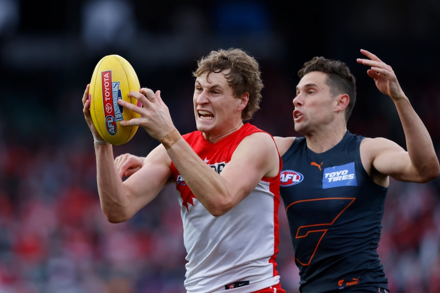 Jordan Dawson catches a yellow AFL ball in front of his face and grimaces