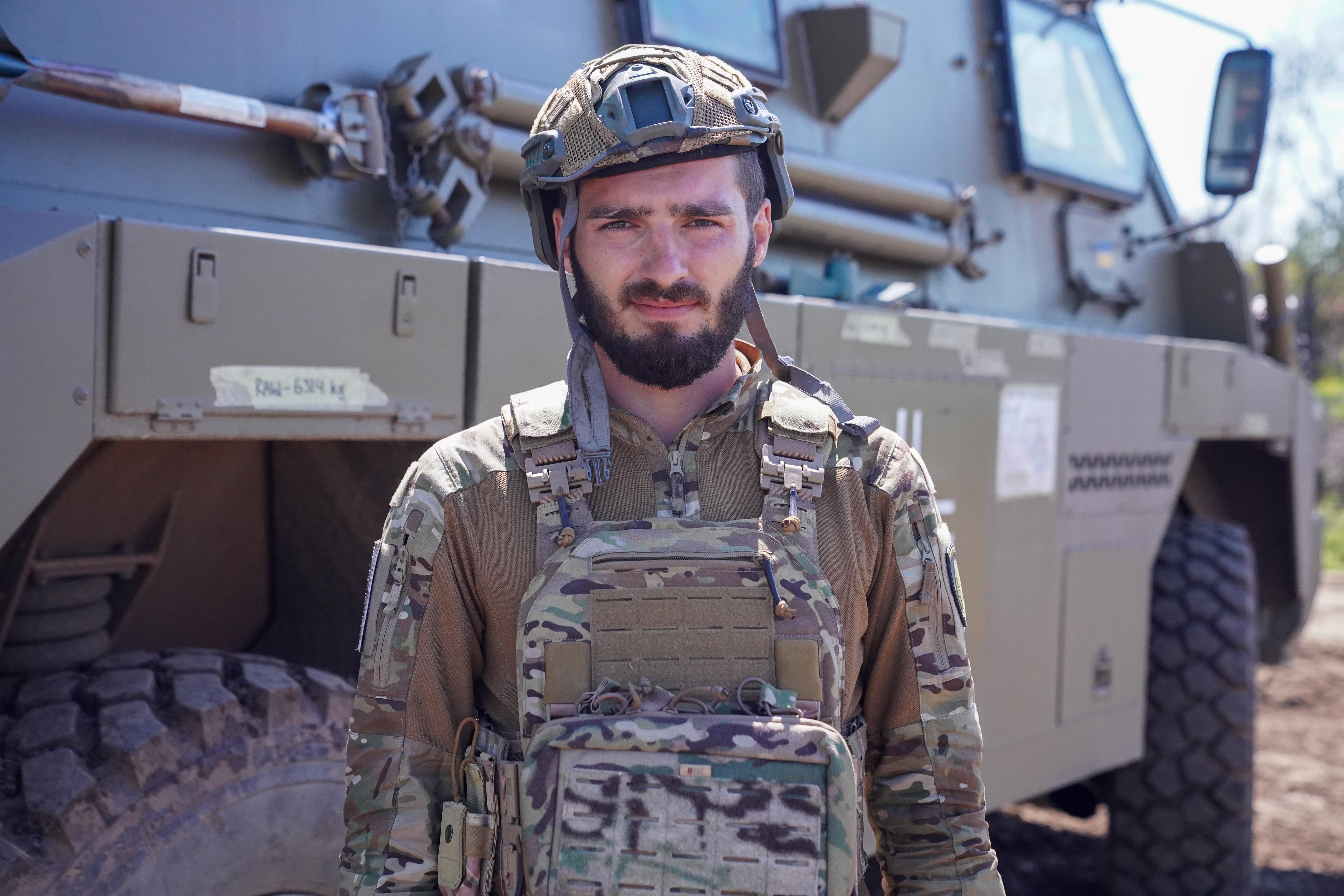 A man in uniform stands in front of a grey-brown vehicle.
