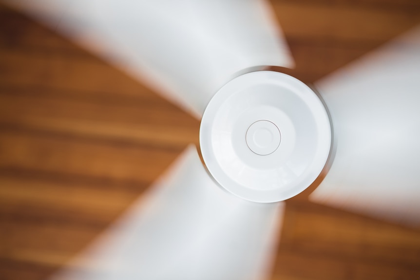 A spinning ceiling fan with three blades for a story about how to reduce the cost of electricity bills over summer.