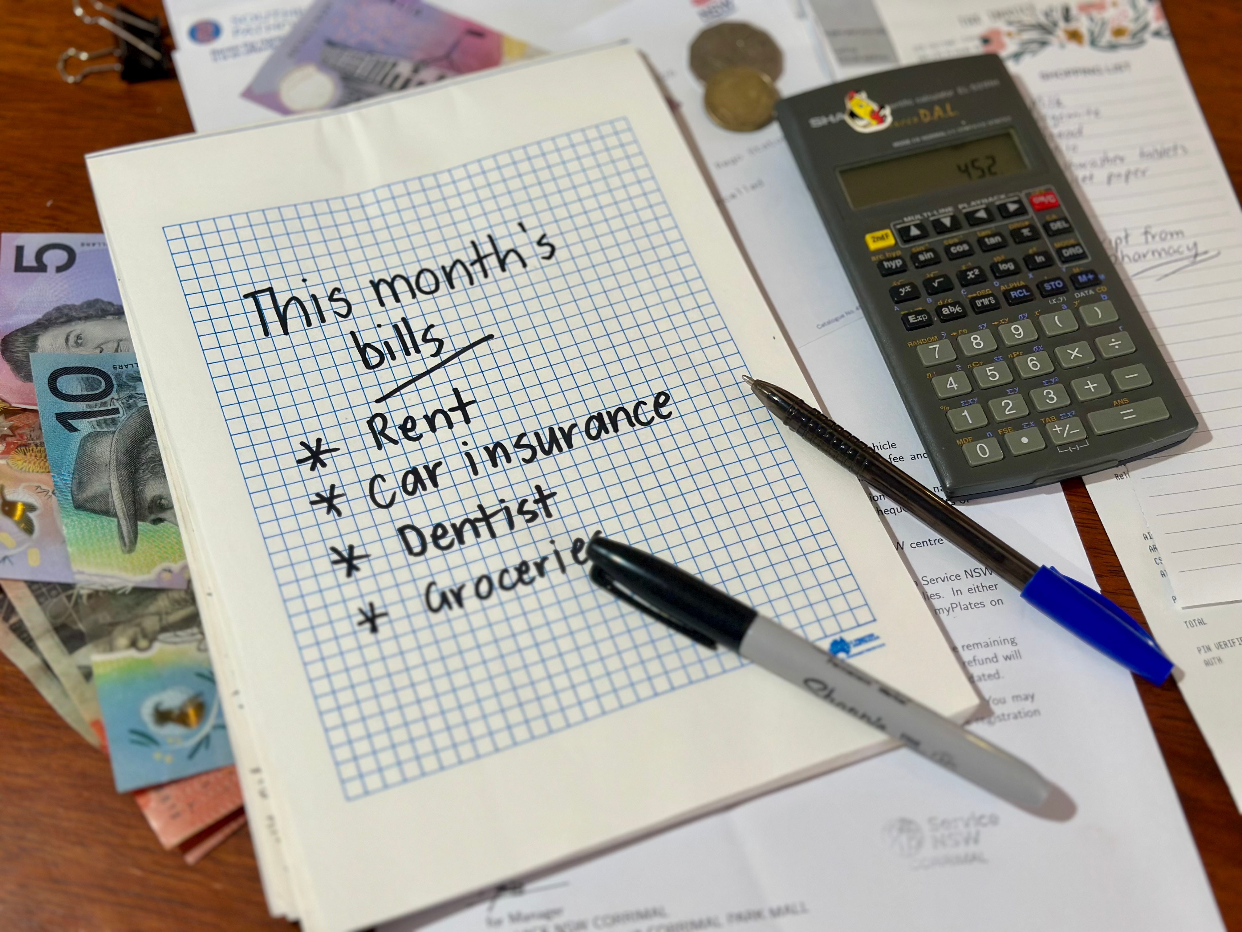 A notebook page listing “This month’s bills” with items like rent, car insurance, dentist, and groceries, next to a calculator.