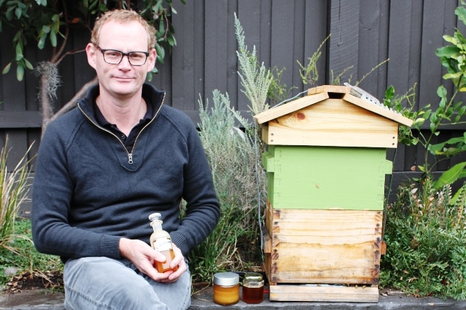 Man sitting in garden with jars of honey and a bee hive