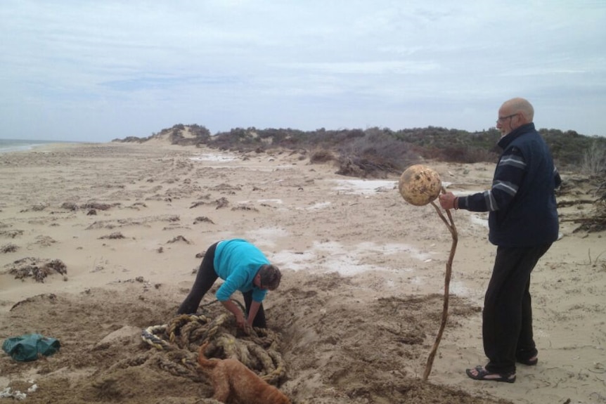 Locals dig a deep hole on the beach to try and uncover metres of rope washed ashore from the farm