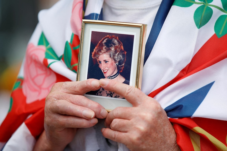 A close up of a person's hands holding a picture of Princess Diana. 
