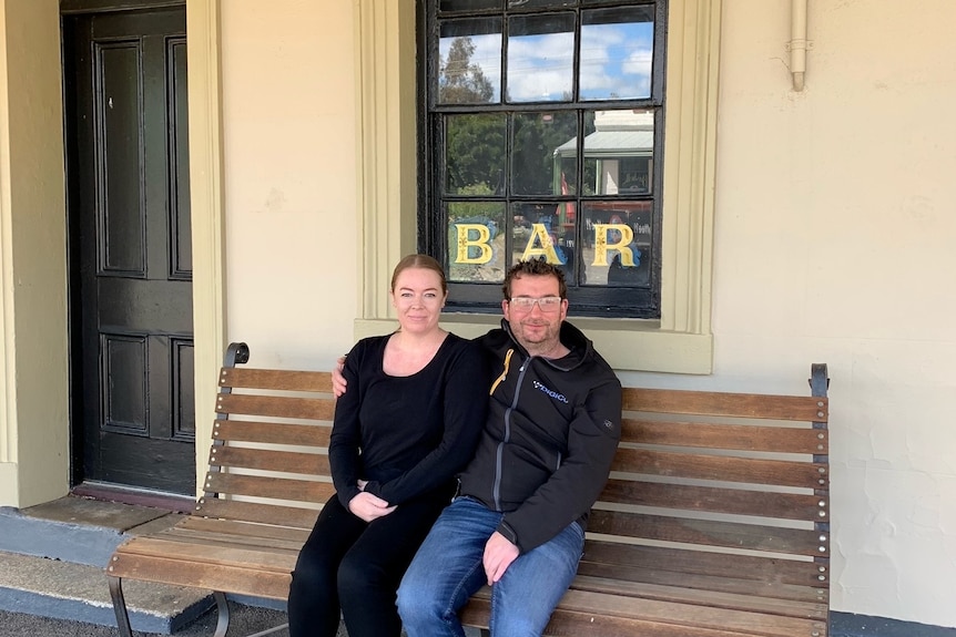 A man and lady sit on an old bench outside an old historic pub.