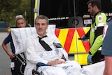 Terry McMaster looks alert as he is wheeled to an ambulance by paramedics.
