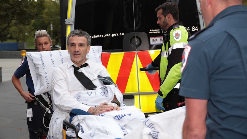 Terry McMaster looks alert as he is wheeled to an ambulance by paramedics.