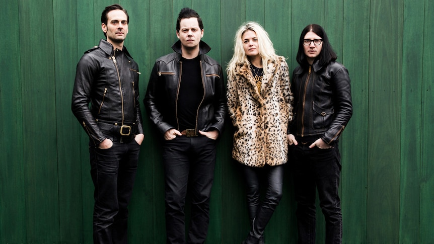 Four members of The Dead Weather standing in front of a green wall
