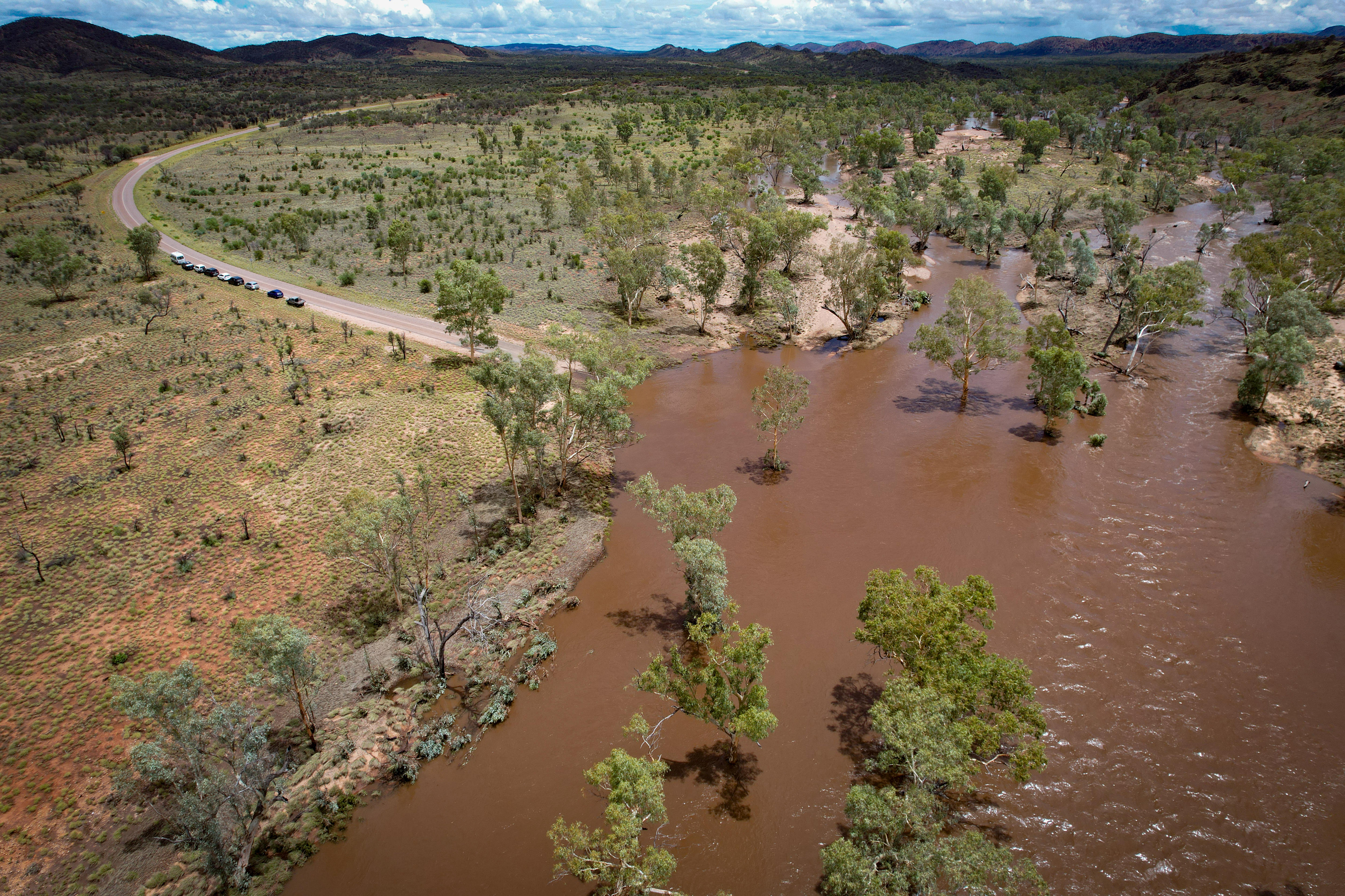 Una carretera interior está cortada por un río marrón inundado.