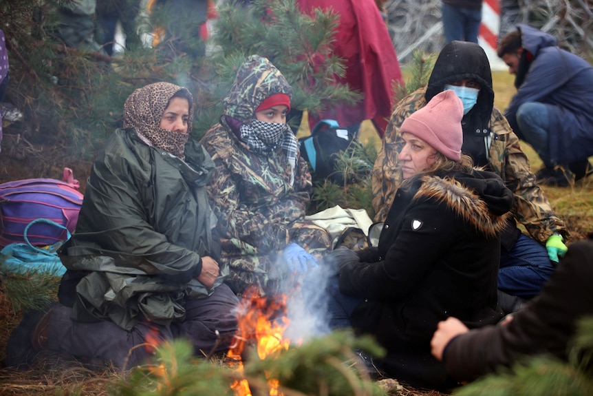 Women in scarves and jackets sit around a fire. 