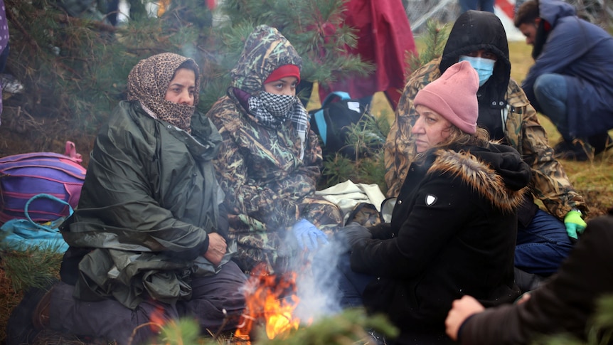 Women in scarves and jackets sit around a fire. 