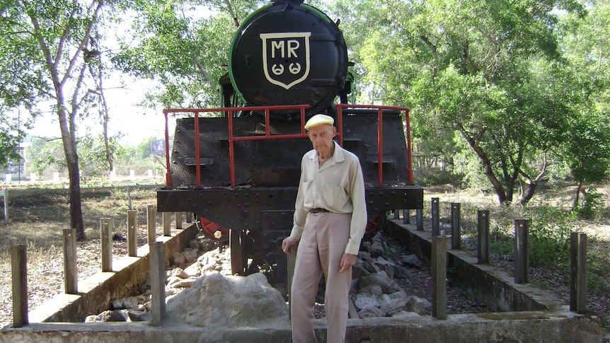 Elderly man stands before a locomotive at a museum