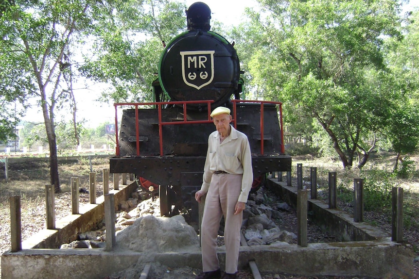 Elderly man stands before a locomotive at a museum
