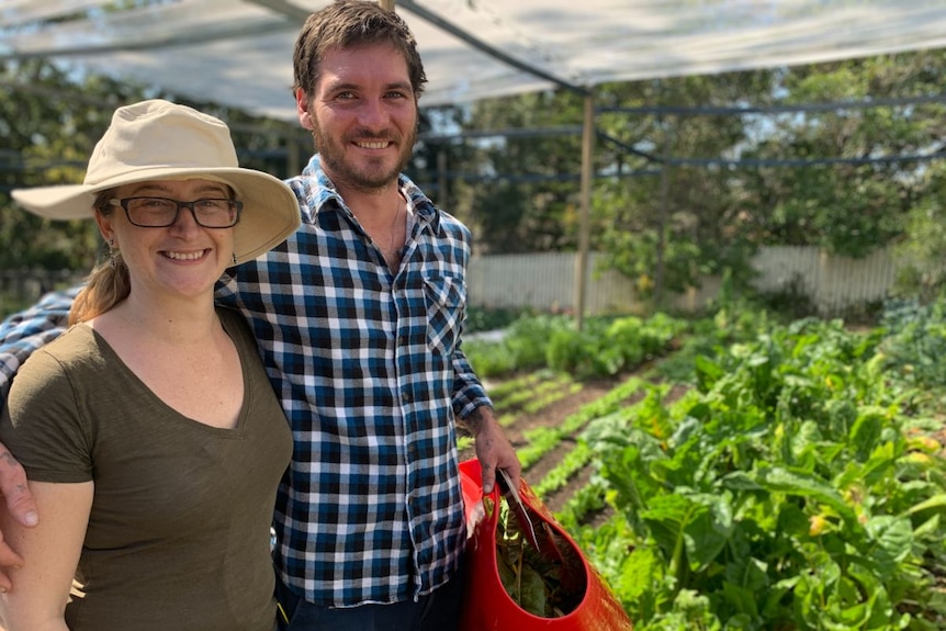 A man and woman smile at the camera with a garden behind them.