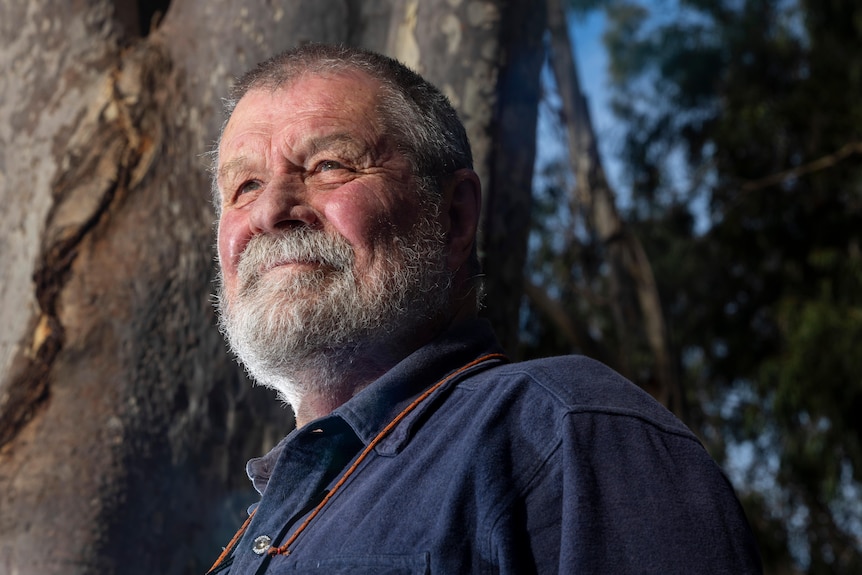 An older man smiling in front of a spotty gum tree