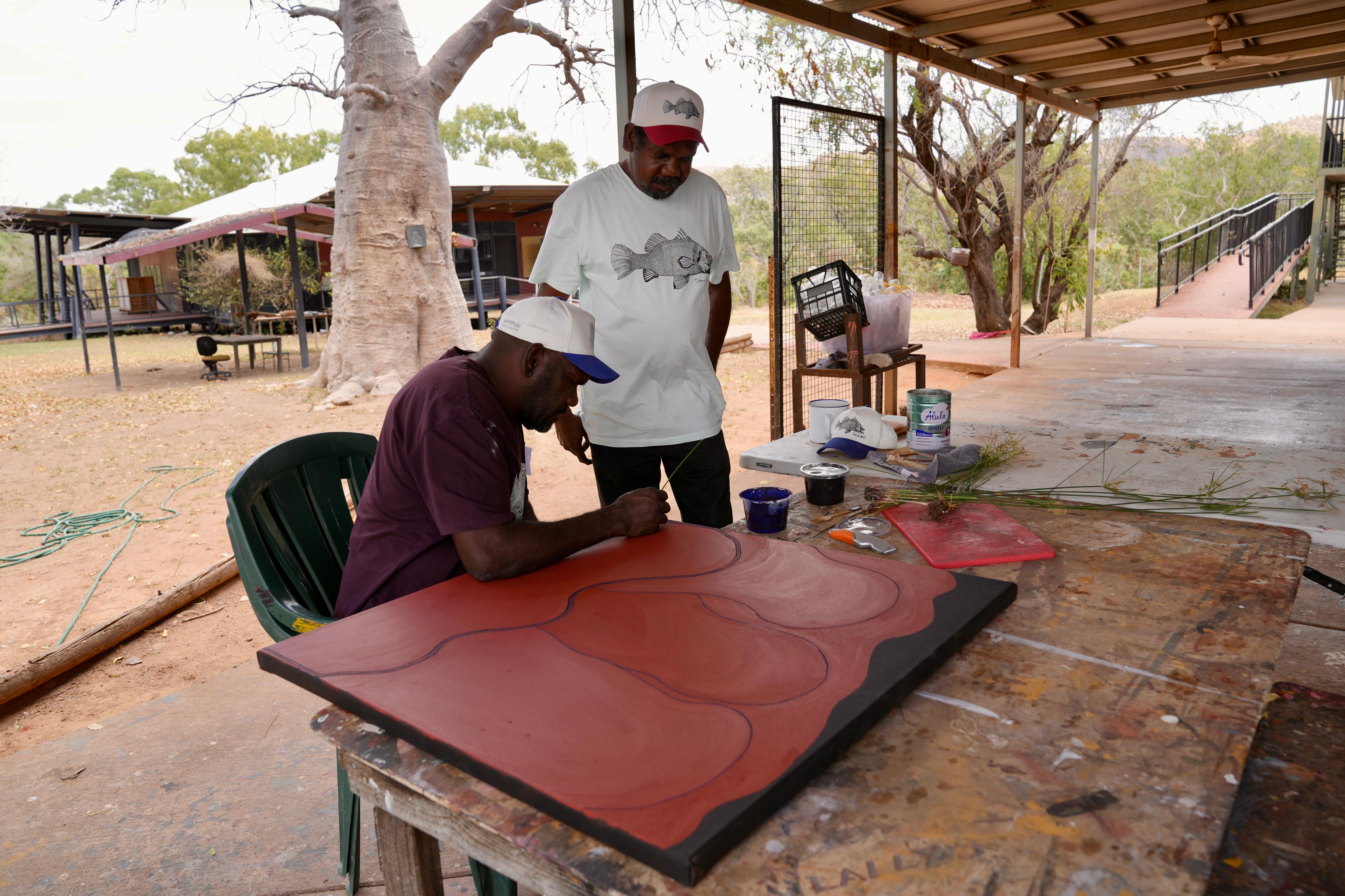 two Aboriginal artists painting together outside
