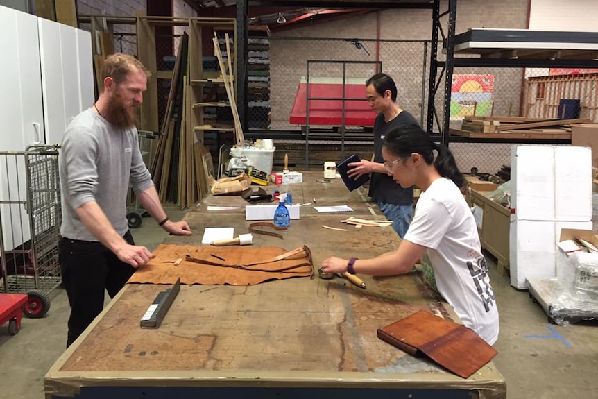 Three people in a workshop making leather folios.