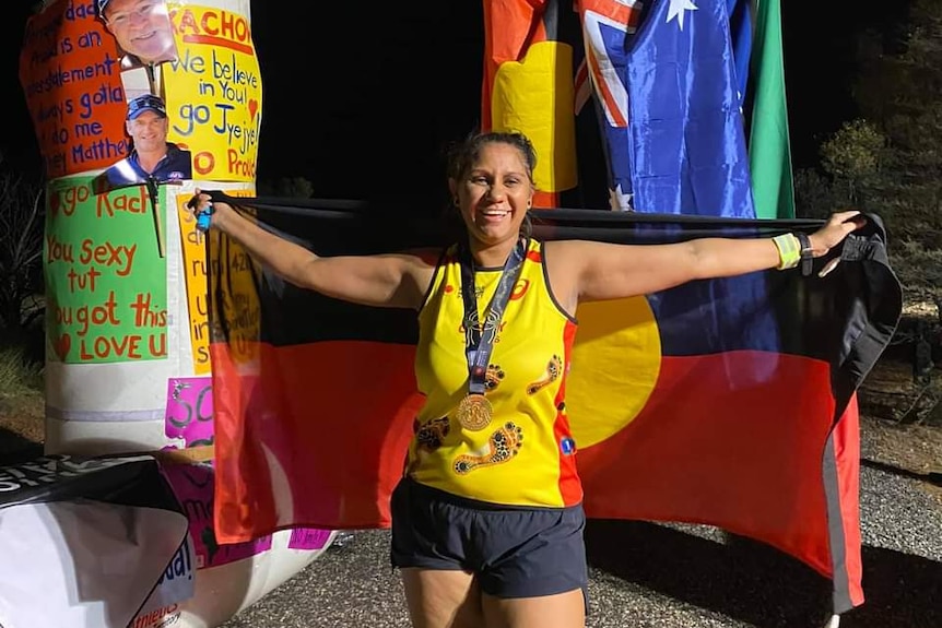 Cecilia Johns holds the Aboriginal flag behind her as she stands in front of an inflatable finish line structure.