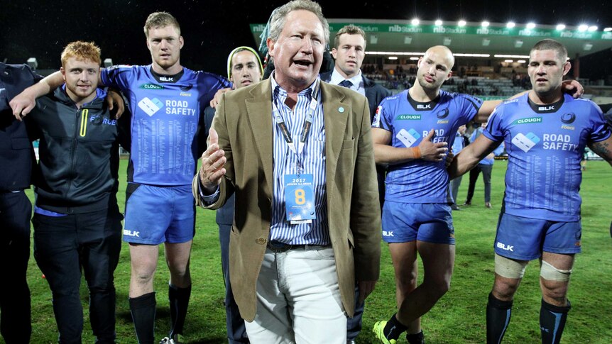 Andrew Forrest stands on Perth Oval talking to Western Force players with some of them behind him with their arms linked.