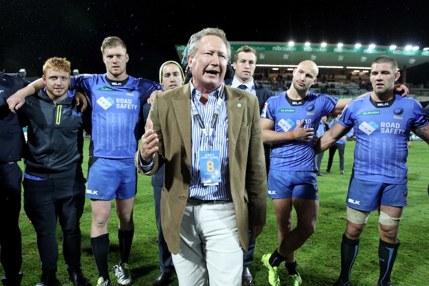 Andrew Forrest stands on Perth Oval talking to Western Force players with some of them behind him with their arms linked.