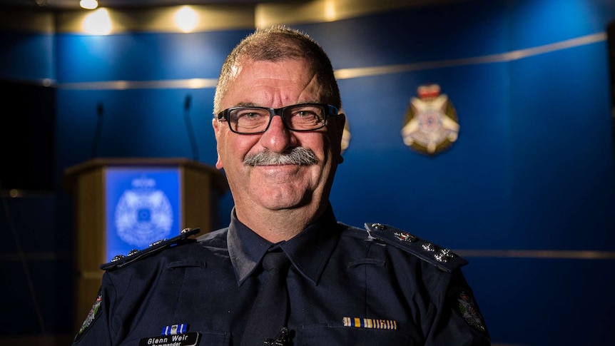 Commander Glenn Weir smiling while standing in room at Victoria Police office.