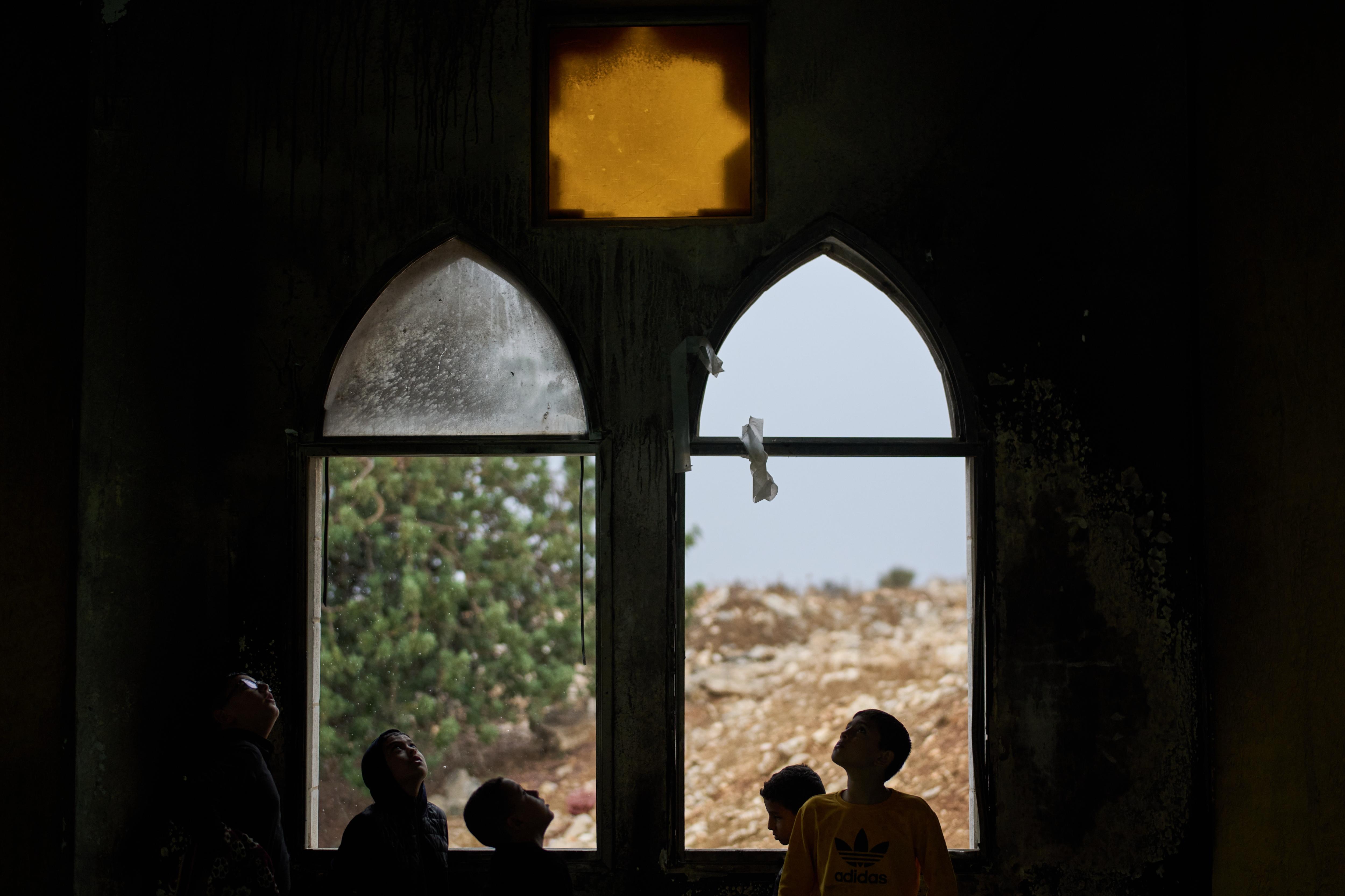 Several Palestinian youths silhouetted at two windows inside a mosque.
