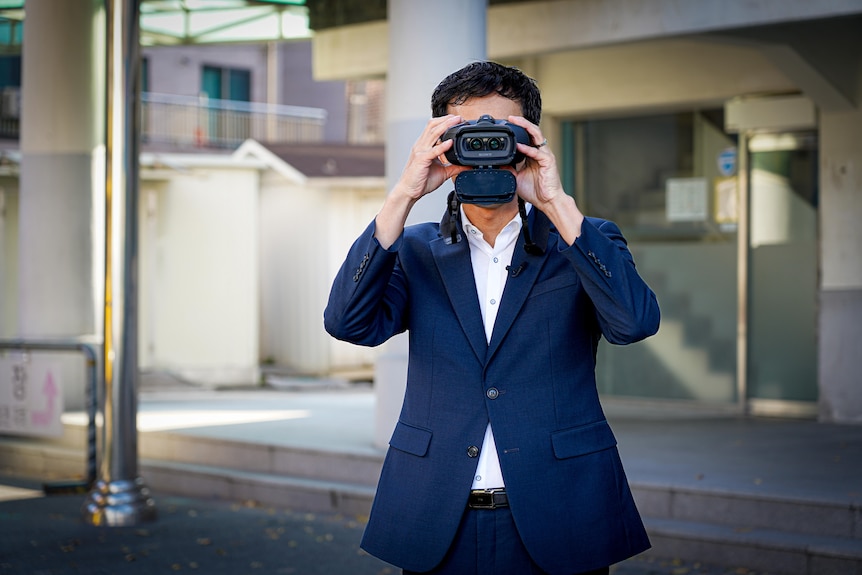 A man in a blue suit holding binoculars to his face