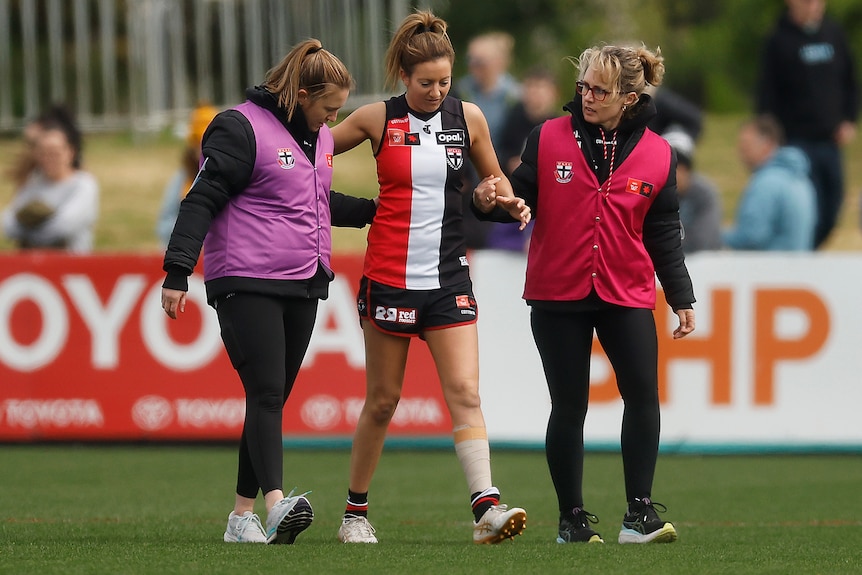 A St Kilda AFLW player is helped from the field after sustaining a knee injury.