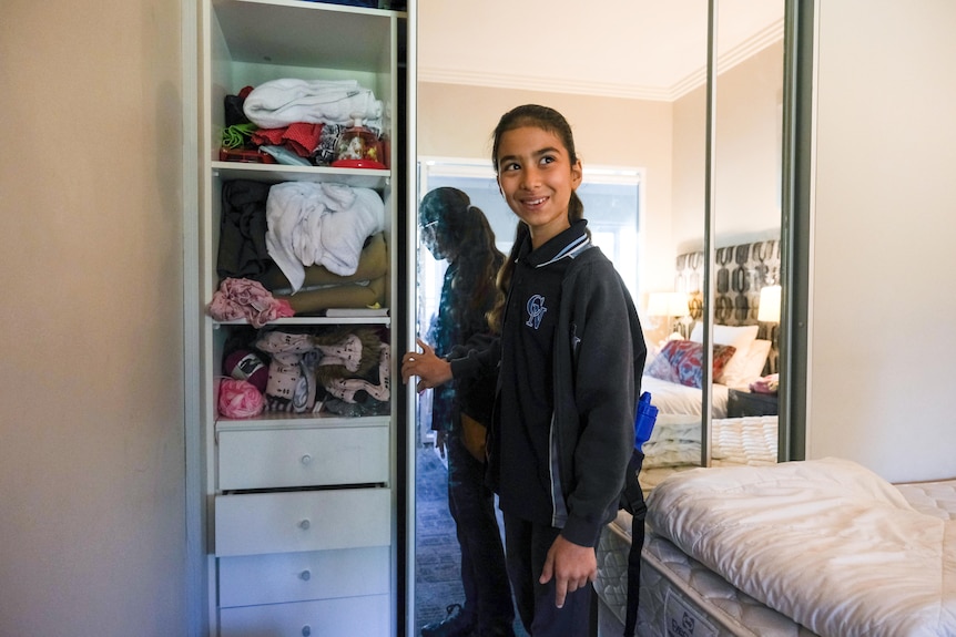 A young girl standing in front of a wardrobe.