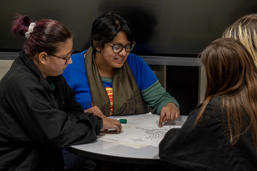 A woman sits talking to three young people.