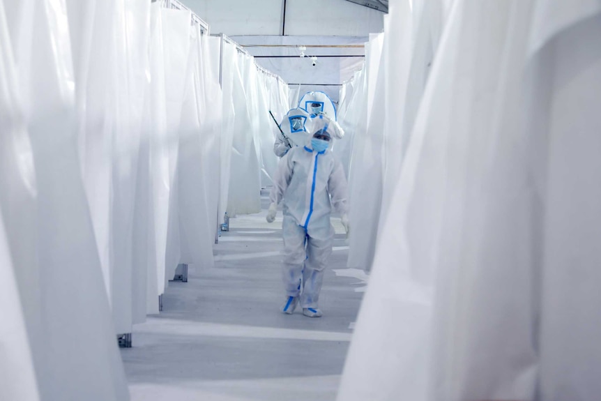 Three health workers in full PPE walking down a corridor made by two white curtains