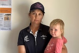 A woman wearing a black polo shirt and cap holding a baby